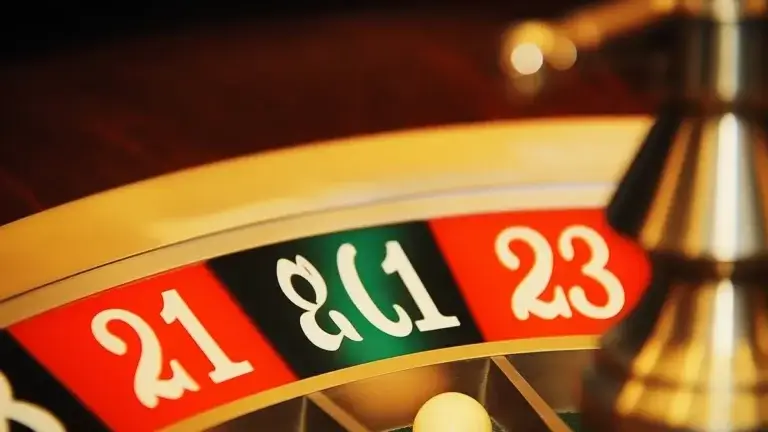 The image is a close-up view of a roulette wheel, focusing on the numbered sections. The numbers 21, 0, and 23 are prominently displayed, with 21 and 23 on red backgrounds and 0 on a green background, as is typical in a European-style roulette wheel. The wheel itself has a metallic sheen, and the white ball is visible, resting in one of the numbered slots. The scene is well-lit, highlighting the vibrant colors and smooth texture of the wheel, creating a sense of anticipation and excitement often associated with the game of roulette.